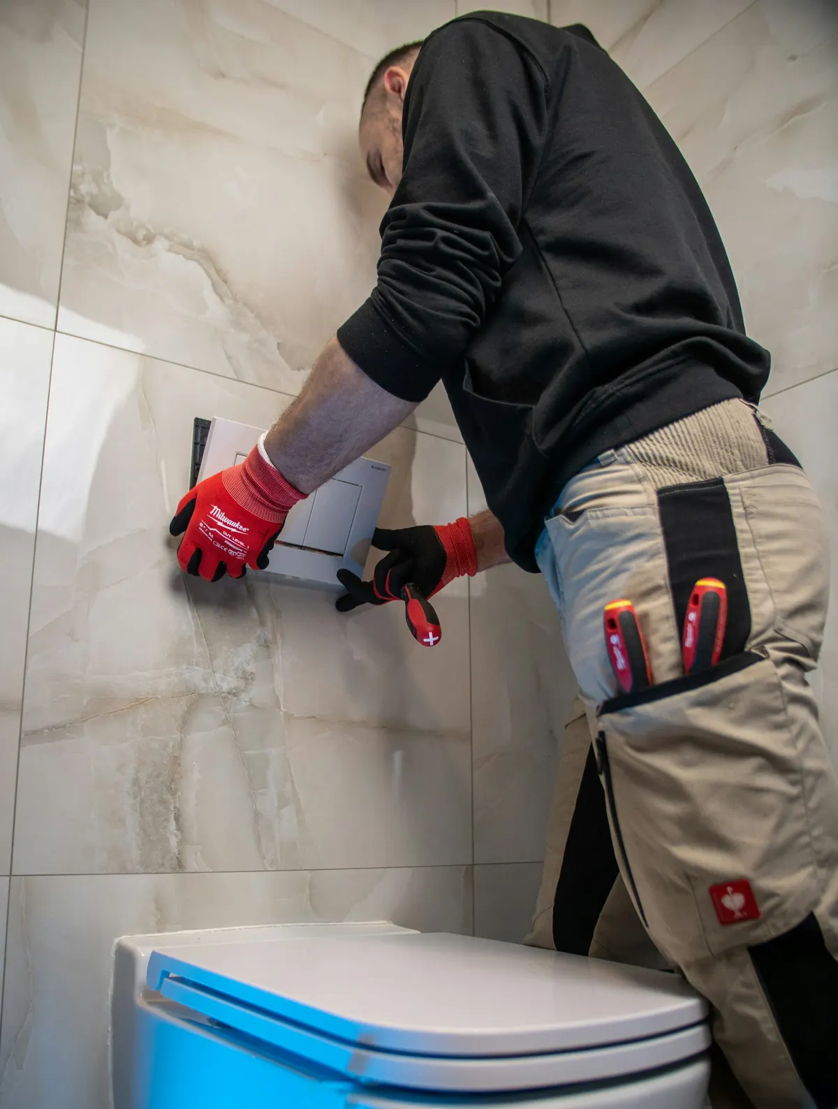 Plumber fitting the flush plate of a wall-hung toilet in a marble bathroom